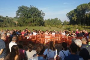 La foto mostra il momento in cui la campagna di scavi è stata mostrata alla comunità. Un gruppo di persone sta osservando i saggi al di fuori delle recinzioni.