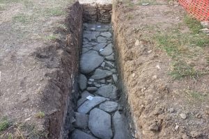 L'immagine mostra il risultato della campagna di scavo sulla città romana. Il saggio rivela una porzione contenente strutture murarie con diverse fasi di vita, prospicienti una strada romana basolata in eccellente stato di conservazione.